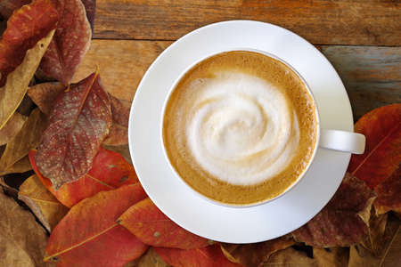 Top view of hot coffee cappuccino cup with milk foam on wood table and autumn leaves background.の写真素材
