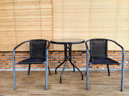 Two black chairs with round table on wood floor, brick wall and bamboo curtainの写真素材