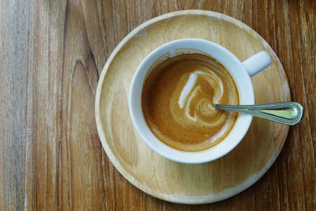 Top view of hot coffee latte cappuccino cup with stirring spoon on wood saucer and table background.の写真素材