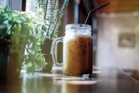 Summer refreshing drinks, cold iced coffee on wood table in relaxing atmosphere coffee shop with blurred indoor potted plants near window.の写真素材