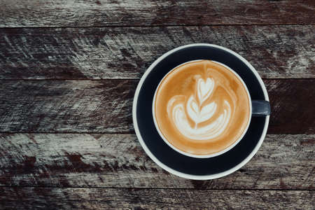 Top view of hot coffee latte cappuccino cup on dark gray ceramic saucer with latte art milk foam on rustic wood planks table background.の写真素材
