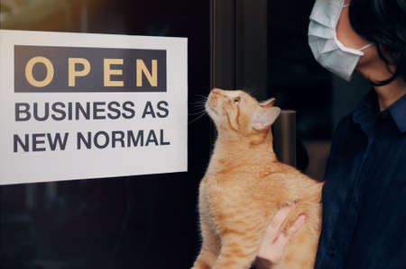 Reopening for business adapt to new normal in the novel Coronavirus COVID-19 pandemic. A cat with their owner person wearing mask in front of business shop with open sign OPEN BUSINESS AS NEW NORMAL"の写真素材