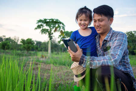 Asian smart farmer father with his happy little girl daughter using digital tablet outdoors in family organic farm.の写真素材