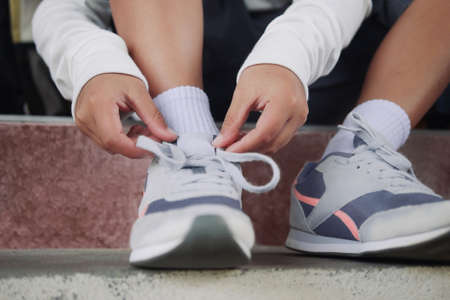 Schoolboy in casual clothing tying shoelaces on sneakers getting ready for school or traveling.