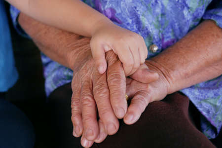 Close-up of small child hand holdiing on elderly person's hand grandmother with Alzheimer and...