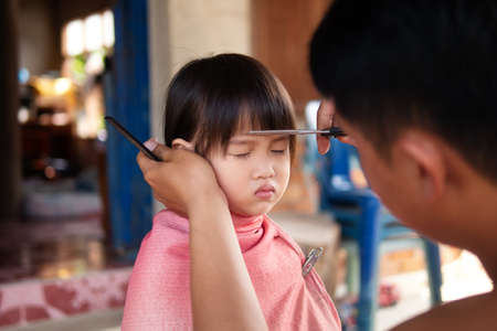 Asian family haircut at home in rural area, little girl getting ready to school getting haircut at home by her father.の写真素材