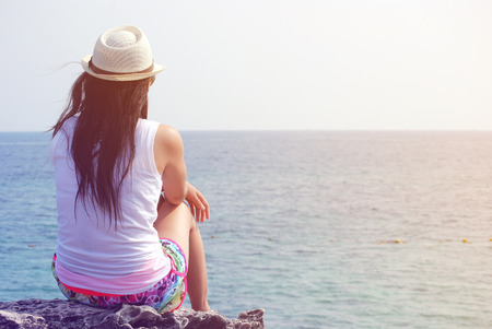 Long hair woman wearing a hat, sitting lonely looking at the sea.の写真素材