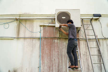 Air conditioner technician is installing the air conditioner on the wall of the house.