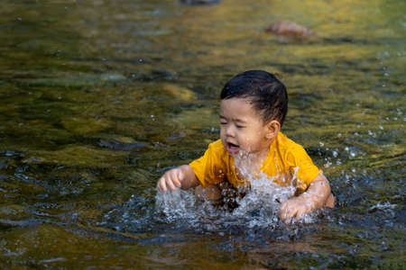 The boy was having fun playing in the water for the first time in the stream.