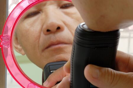 the Man who shaving with an Electric Shaver front the Mirrorの写真素材