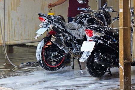 A Worker who washing motorcycle with water pipe and Sponge