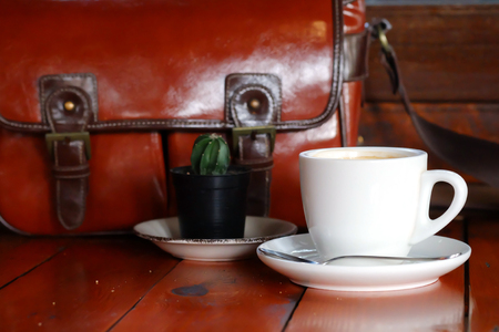 Hot Black Americano coffee in white cup with vintage brown leather bag on teak wooden background. have some space for write wordingの写真素材