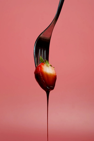 fondue strawberry soaked in hot black chocolate on a fork with pink background with minimalist style .have some spec for write wordingの写真素材