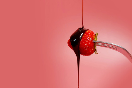 fondue strawberry soaked in hot black chocolate on a fork with pink background with minimalist style .have some spec for write wordingの写真素材