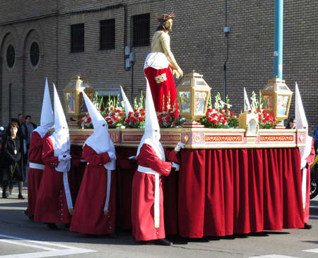 Nazarene penitents in red and white with a Jesus Christ Holy Passion float during Easter holy Week...