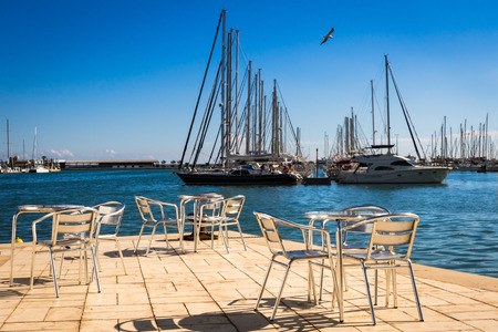 Metal furniture by the sea on a bright sun against the moored yachts.の写真素材