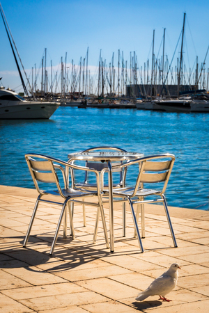 Metal furniture by the sea on a bright sun against the moored yachts.の写真素材