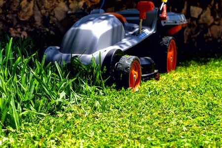 The gray mower with orange wheels on an emerald grass in the course of work.