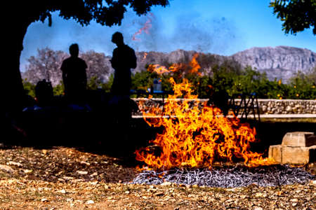 An evening bonfire with silhouettes of people and a mountain range in the background.の写真素材