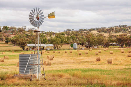 windmill in the field with hay and straw bales in the end of summerの写真素材