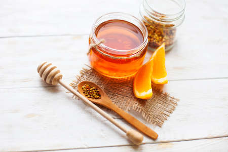 Honey in a glass jar and orange on a white background wooden rustic . Selective focus .の写真素材