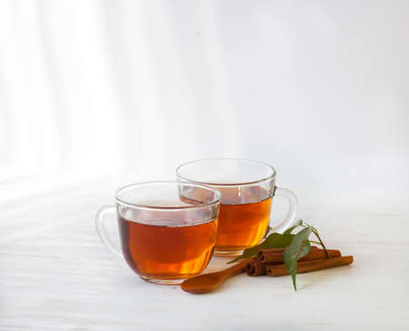 Glass cup of black tea with cinnamon sticks on a white background wooden table.の写真素材