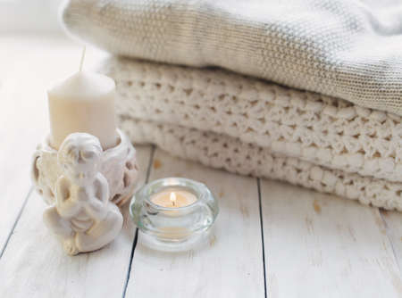 Stack of cozy knitted sweaters and candle on a tableの写真素材