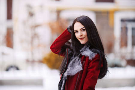 Sunny frozen morning of fashionable young woman smiling on winter street full of snow. Amazing girl in warm winter clothes enjoying cold weather on red telephone box background Place for textの写真素材
