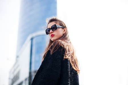 Fashion portrait of young elegant confident woman outdoor. black jacket, red lips and sunglasses.On the background of the big city.の写真素材