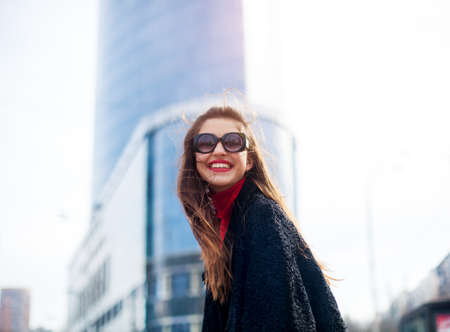Expressive girl with long hair having fun in city Cool girl with long hairstyle and red lips She wears sunglasses and smiling to camera with snow-white smile.の写真素材