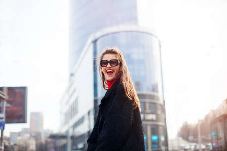 Cool girl with long hairstyle and red lips having fun in the city. She wears sunglasses and smiling to camera with snow-white smile.の写真素材