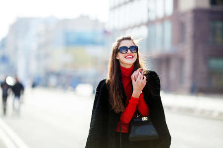 Beautiful amazing brunette woman with long wavy hairstyle in spring or fall stylish urban outfit walking on the street. Red lips, slim body. she smiles and looks at the cameraの写真素材