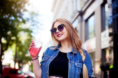 Cool girl with long hairstyle and red lips having fun in the city. She wears sunglasses and retro...