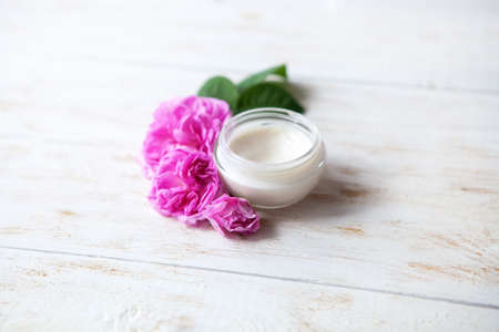Pot of beauty cream surrounded by flowers on white wooden table Cosmetics for care