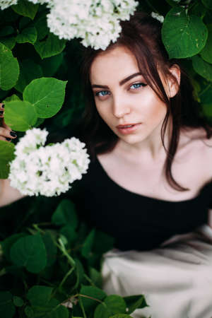 Fashion style beauty romantic portrait of young pretty beautiful woman with long hair posing between white hydrangeas. Stunning girl looking at you or in camera.Closeupの写真素材