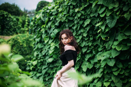 Beautiful princess in a long dress and black hair , walk through the gardens Stunning girl looking at you or in cameraの写真素材