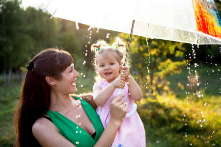 Happy funny family with umbrella under the autumn shower. Girl and her mother are enjoying rainfall. Kid and mom are playing on the nature outdoors.の写真素材