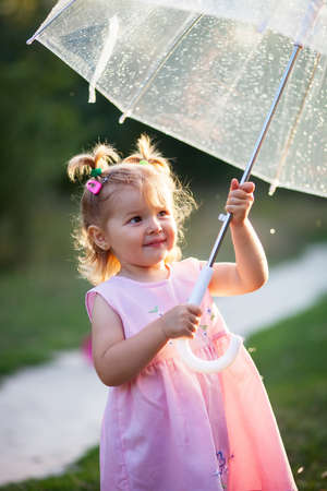 young girl enjoying the rain Cute little toddler girl standing on the nature outdoors. Close up portrait of Pretty little girl under umbrella in the parkの写真素材
