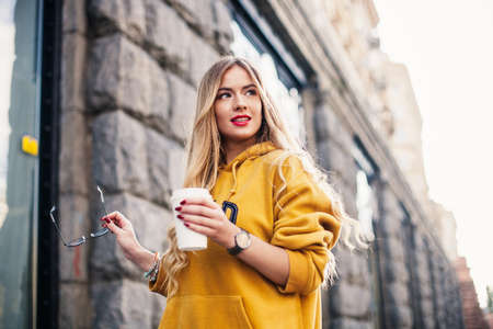 Pensive blond woman posing on modern streets, drinking coffee or cappuccinoの写真素材