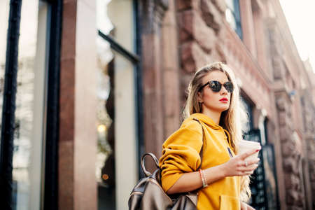 Outdoor waist up portrait of young beautiful woman with long hair. Model wearing stylish sunglasses, clothes, holding bag. City lifestyle. Copy space for textの写真素材