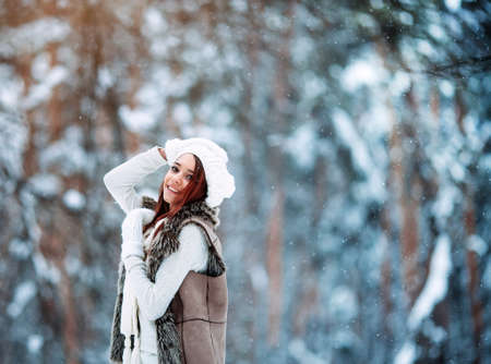 Beautiful girl in white clothes having fun outdoor in winter forest under snowflakes. copyspace area for sloganの写真素材
