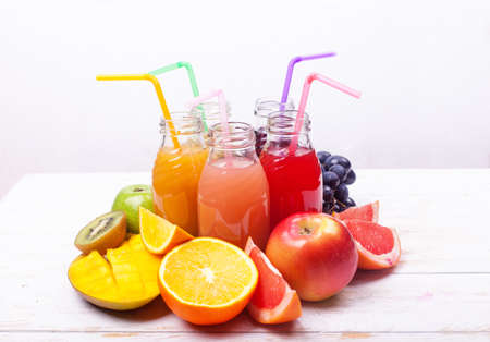 Row Fresh Juices Smoothie five Bottles Red Green pink burgundy Yellow Color Fruits Melon Apple Kiwi Grapes Orange Mango Pomegranate Tropical Selective focus white Wooden Table.の写真素材