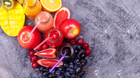 Fresh Color Juices Smoothie Violet Green Yellow Orange Red from Tropical Fruits Kiwi Water Melon Apple Orange Banana Pine Apple Mango Pomegranate Grape Bottles Rainbow Dark Background.の写真素材