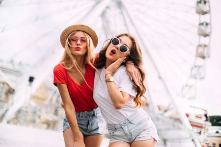 happy smiling pretty girls having fun.stylishly dressed in short denim shorts and bright t-shirts, sunglasses.posing on the background of a ferris wheelの写真素材