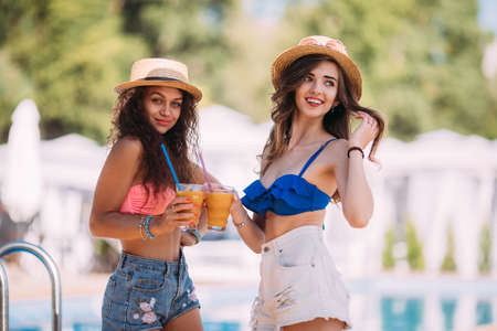 portrait of young sexy pretty woman drinking tasty cocktail, bright summer outfits and accessories Best friends laugh and go crazy background of the pool.の写真素材
