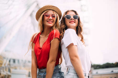 Closeup portrait happy smiling pretty girls having fun.stylishly dressed in short denim shorts and bright t-shirts, sunglasses.posing on the background of a ferris wheelの写真素材