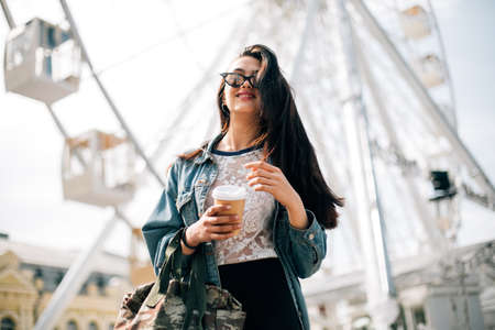 young stylish girl enjoys summer and vacation. Brunette in trendy sunglasses walks in the cityの写真素材