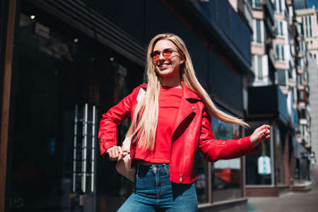 Well-dressed lady in good mood playfully posing on city background.Outdoor portrait of cute blonde...