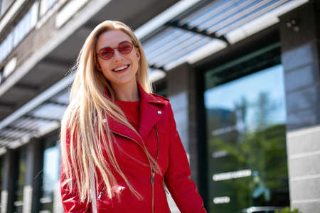 young stylish girl enjoys summer and vacation.Outdoor portrait of cute blonde lady wears elegant red...
