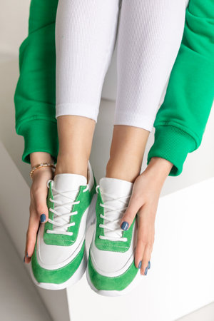 Close up trendy spring fashion outfit .female hands holding white green sneakers. Stylish womens sports shoes. fashionの写真素材